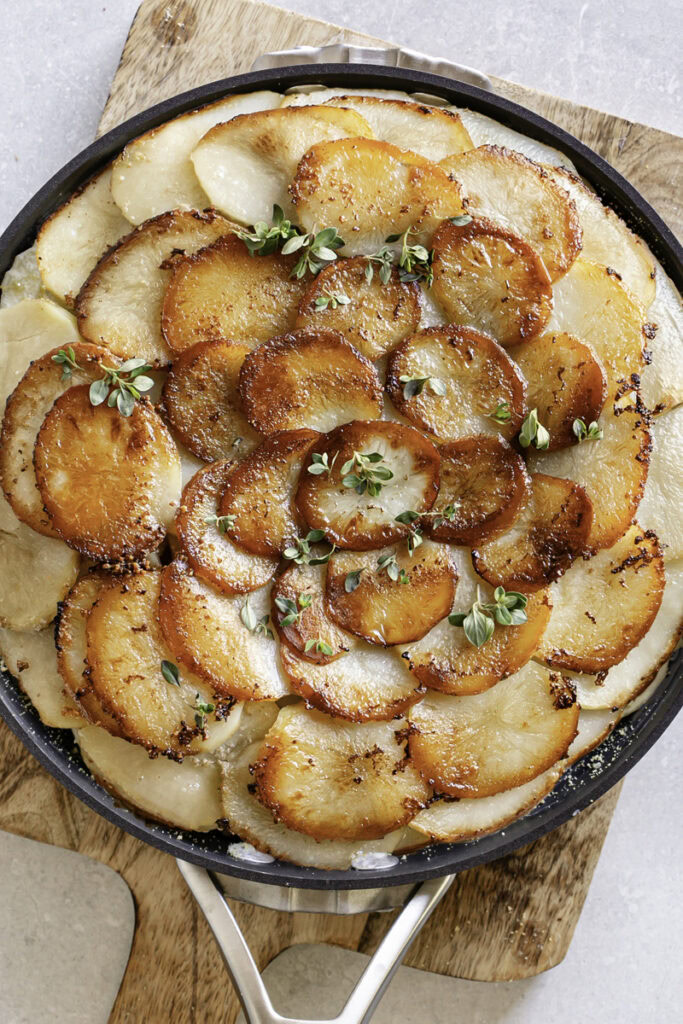 baked Pommes Anna skillet potatoes in a skillet garnished with fresh thyme