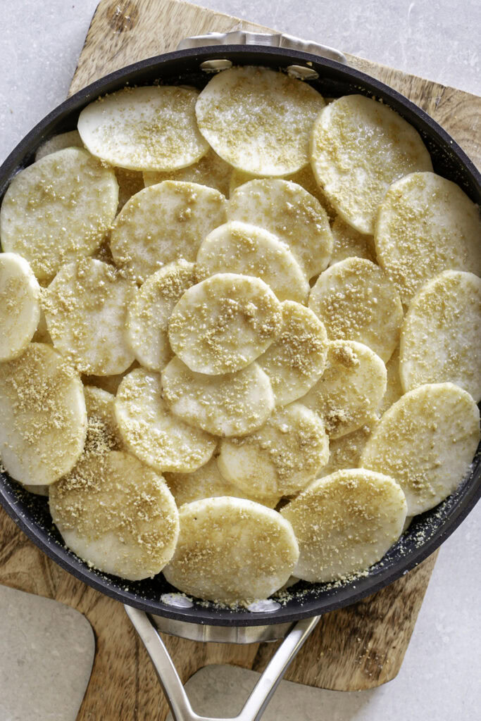 uncooked potato slices in a skillet drizzled with butter and garnished with parmesan cheese