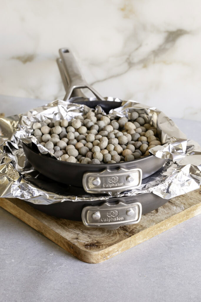 two skillets stacked on top of one another with foil over the potatoes in the bottom skillet to press them down, pie weights in the top skillet