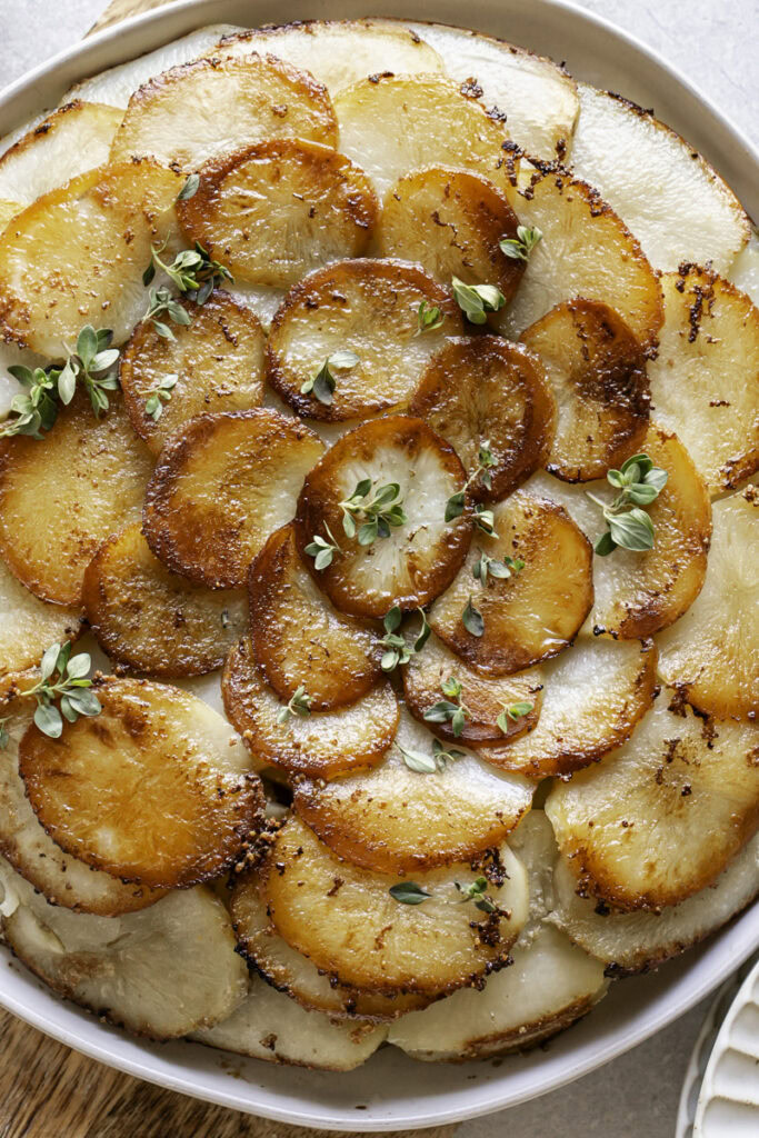 a close up of Pommes Anna skillet potatoes garnished with fresh thyme
