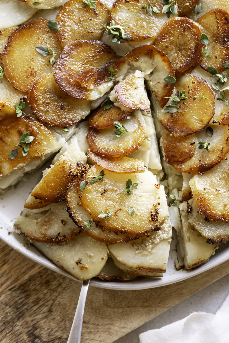 a close up of Pommes Anna skillet potatoes on a plate sliced with a serving spatula under the slice