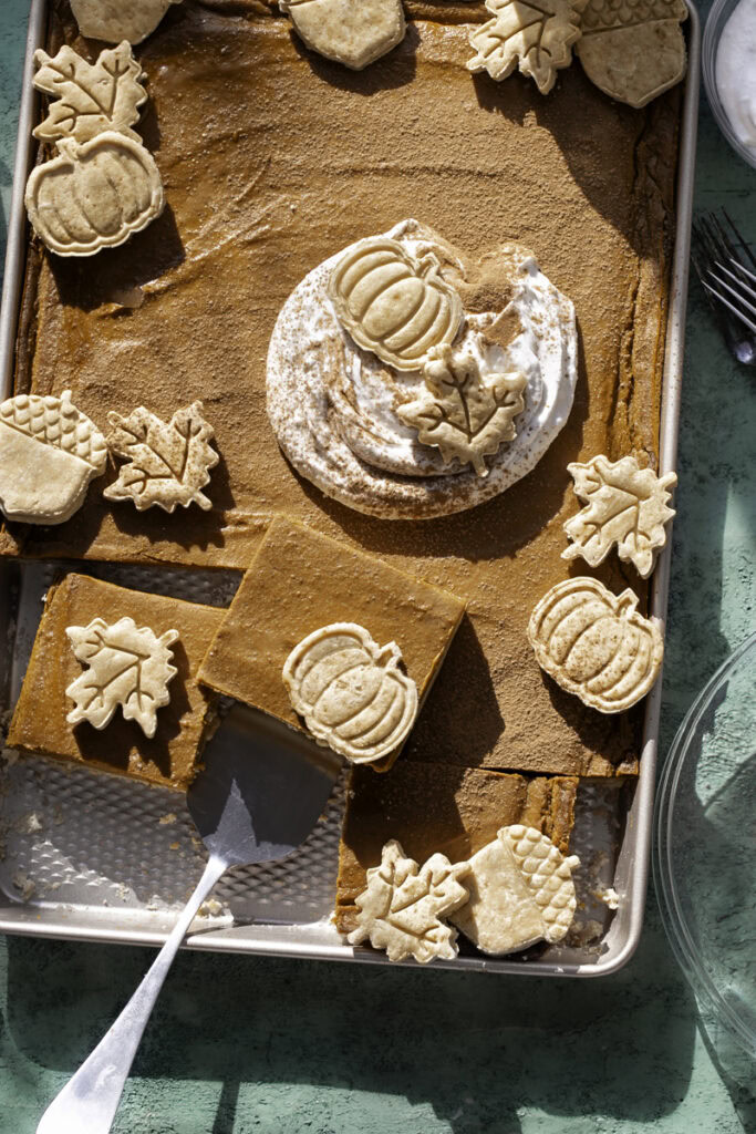 Sheet Pan Pumpkin Pie, decorated with a dollop of whipped cream and pie crust cut outs. The bottom half of the pie is sliced into squares