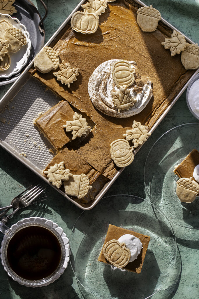 sheet pan pumpkin pie sliced into squares, two pieces served onto glass plates with a dollop of whipped cream and a pie crust cut out.