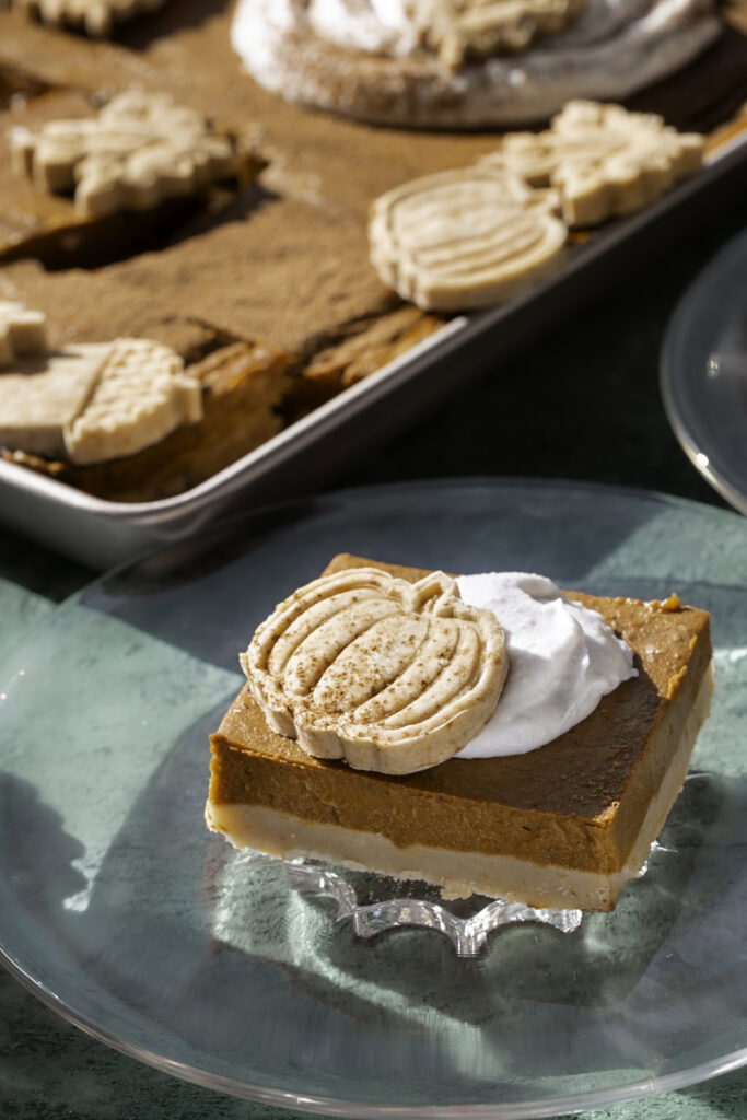 a close up of a slice of sheet pan pumpkin pie on a glass plate with a dollop of whipped cream and a pie crust cut out