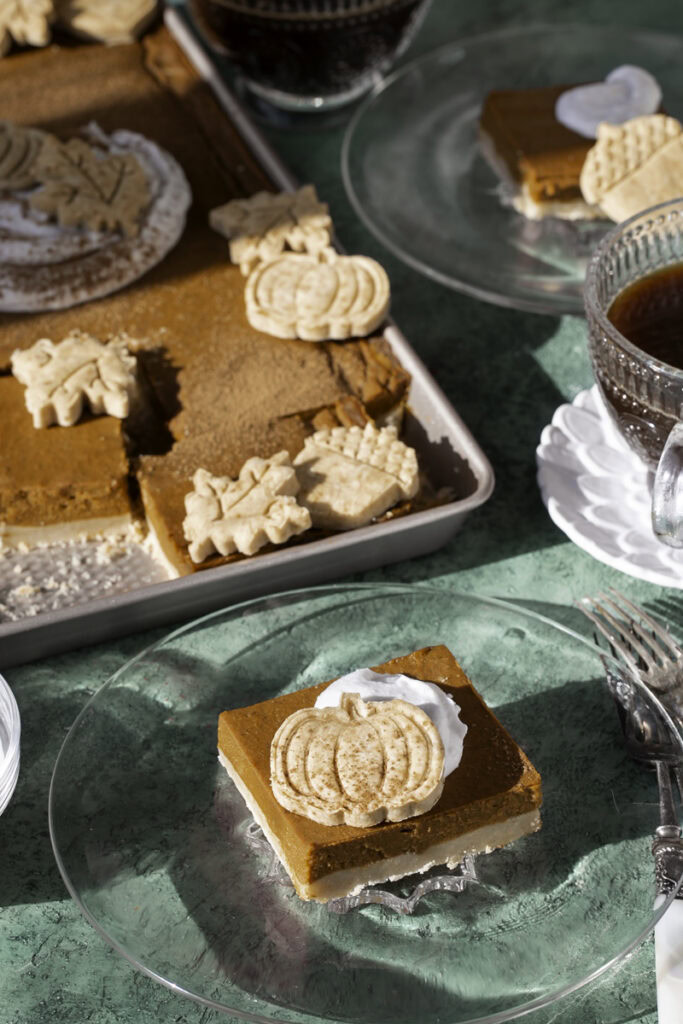 sheet pan pumpkin pie sliced into squares, two pieces served onto glass plates with a dollop of whipped cream and a pie crust cut out