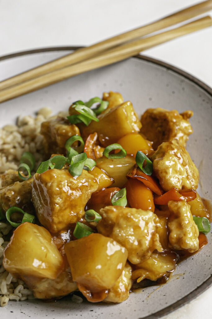 extreme close up of a bowl of 30 Minute Sweet & Sour Tofu with wooden chopsticks resting on the bowl