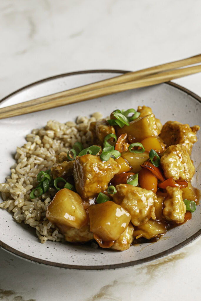 3/4 shot of a bowl of 30 Minute Sweet & Sour Tofu with wooden chopsticks resting on the bowl