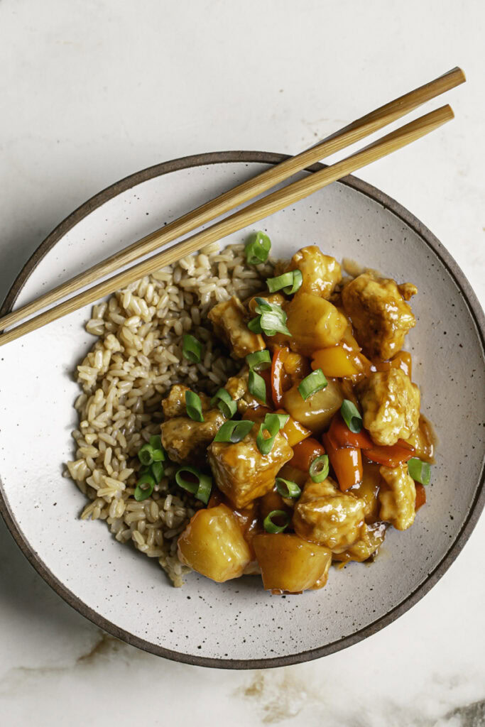 a bowl of 30 Minute Sweet & Sour Tofu garnished with fresh green onion and wooden chopsticks resting on the bowl