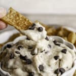 action shot of a cinnamon churro chip scooping some High Protein Vegan Cannoli Dip out of the bowl
