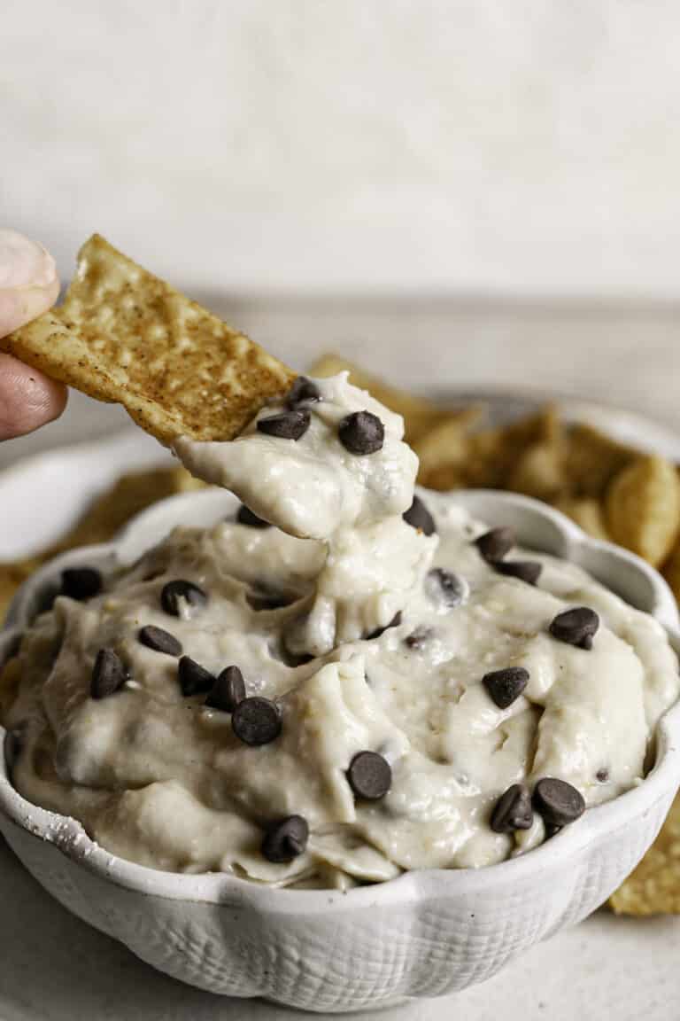 action shot of a cinnamon churro chip scooping some High Protein Vegan Cannoli Dip out of the bowl