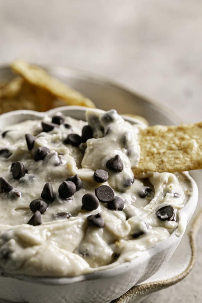 a close up shot of a bowl of High Protein Vegan Cannoli Dip with cinnamon churro chips around it, one with dip on it sticking out of the bowl