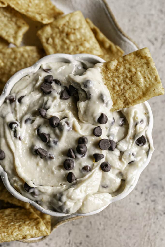 a bowl of High Protein Vegan Cannoli Dip with cinnamon churro chips around it, one with dip on it sticking out of the bowl