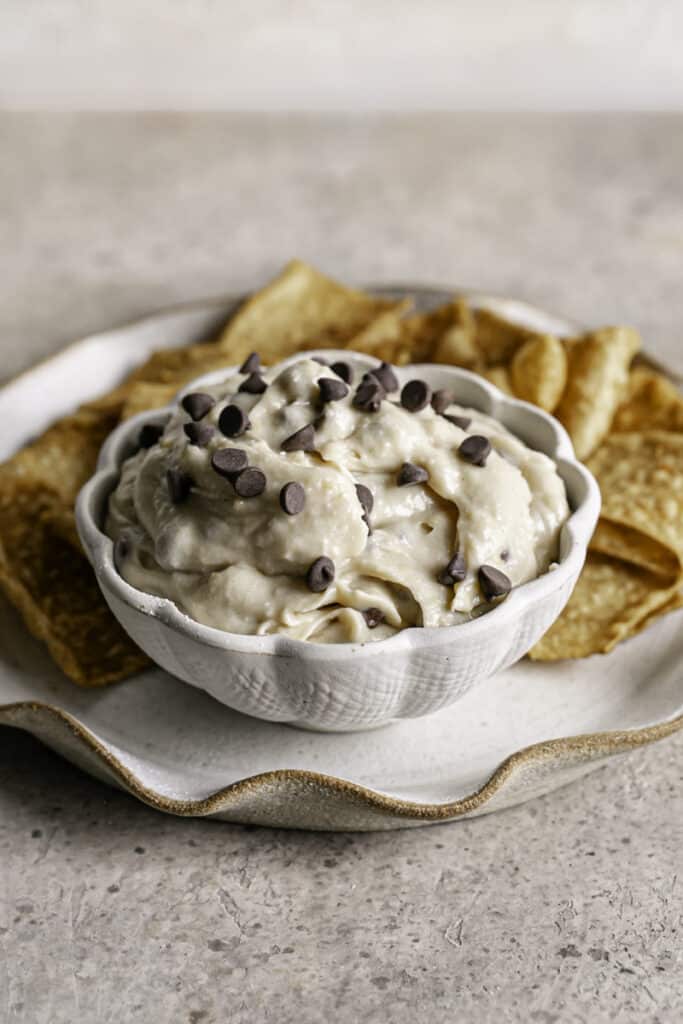 3/4 shot of a bowl of High Protein Vegan Cannoli Dip on a plate with cinnamon churro chips around it