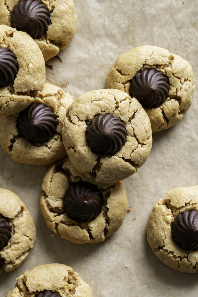 a close up overhead shot of Almond Flour Peanut Butter Blossom Cookies on parchment paper, some stacked on top of one another.