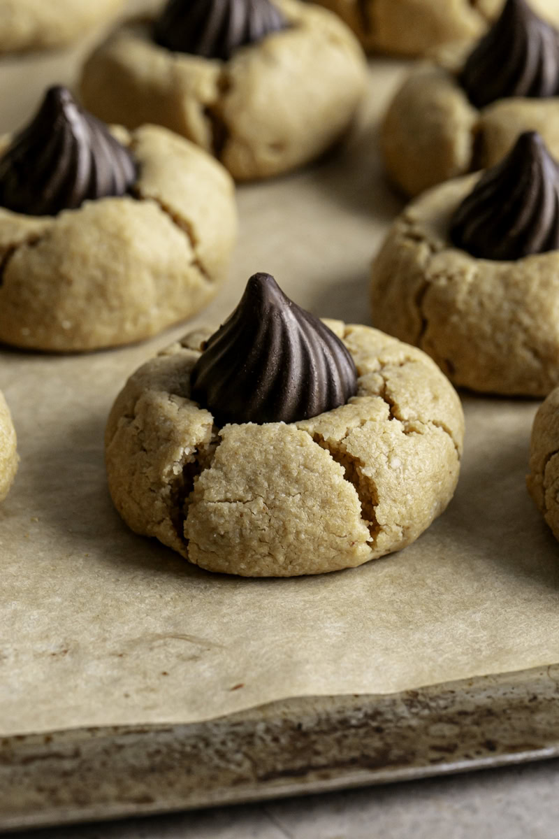 a close up of a Almond Flour Peanut Butter Blossom Cookie on a parchment lined baking sheet
