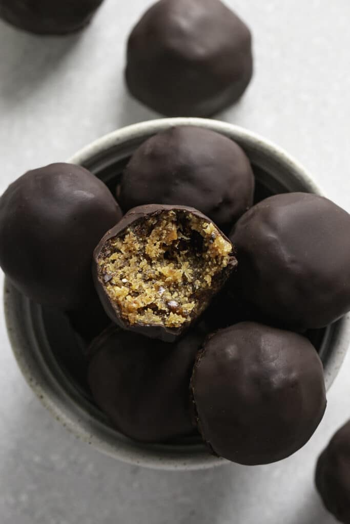 an overhead shot of Chocolate covered Peanut Butter Almond Flour Date Bites in a small bowl, the top one with a bite taken out of it