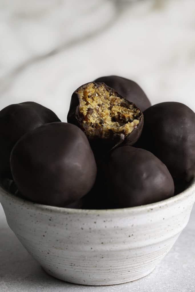 a close up of Chocolate covered Peanut Butter Almond Flour Date Bites in a small bowl, the top one with a bite taken out of it.