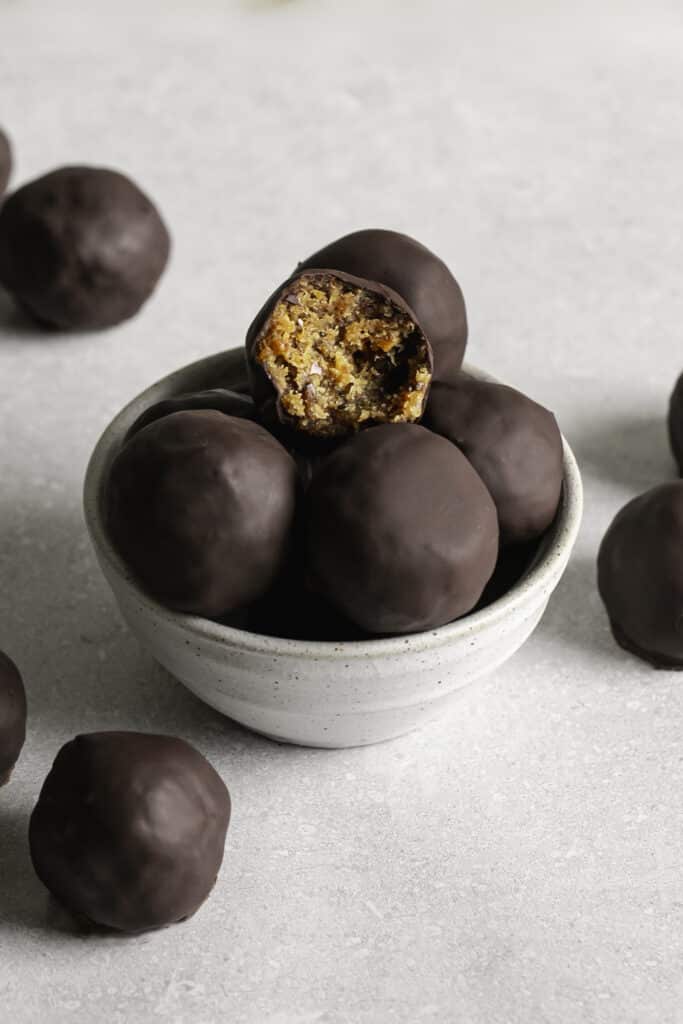 Chocolate covered Peanut Butter Almond Flour Date Bites in a small bowl, the top one with a bite taken out of it.
