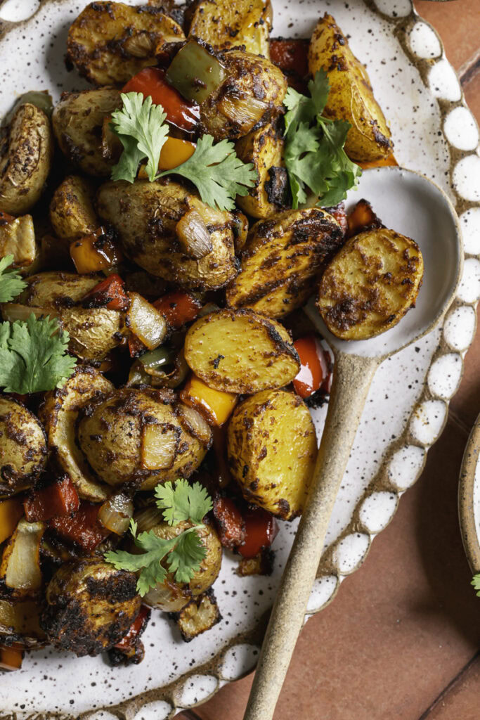 a close up overhead photo of fajita roasted potatoes on an oval ceramic plate with a spoon.