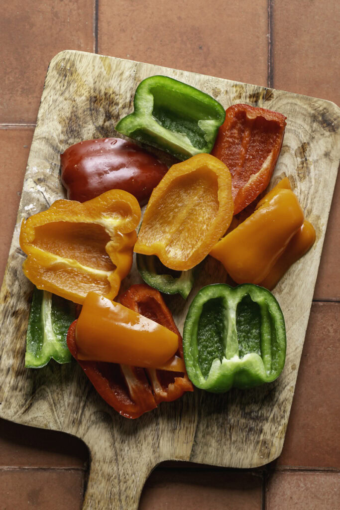 cut red, orange, and green bell pepper on a wooden cutting board.