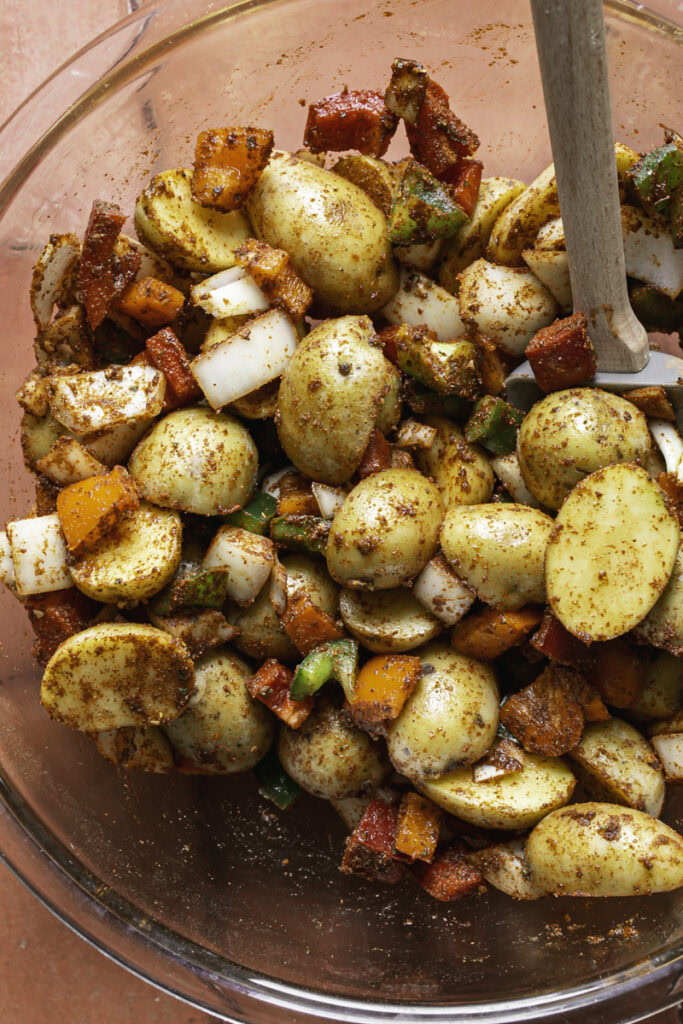 potatoes, bell pepper, onion, olive oil, and taco seasoning tossed together in a large glass bowl with a spatula.