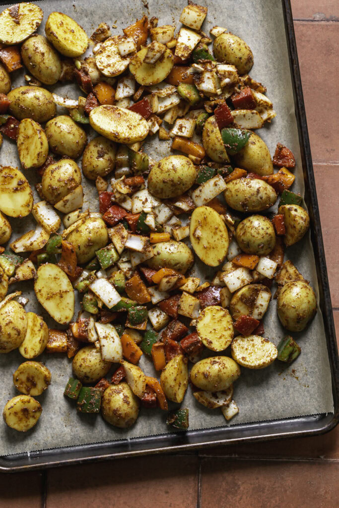 potatoes combined with bell pepper, onion, and taco seasoning spread out on a parchment-lined baking sheet ready to be roasted in the oven.