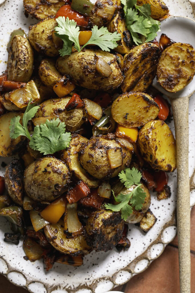 a close up overhead photo of fajita roasted potatoes on an oval ceramic plate with a spoon.