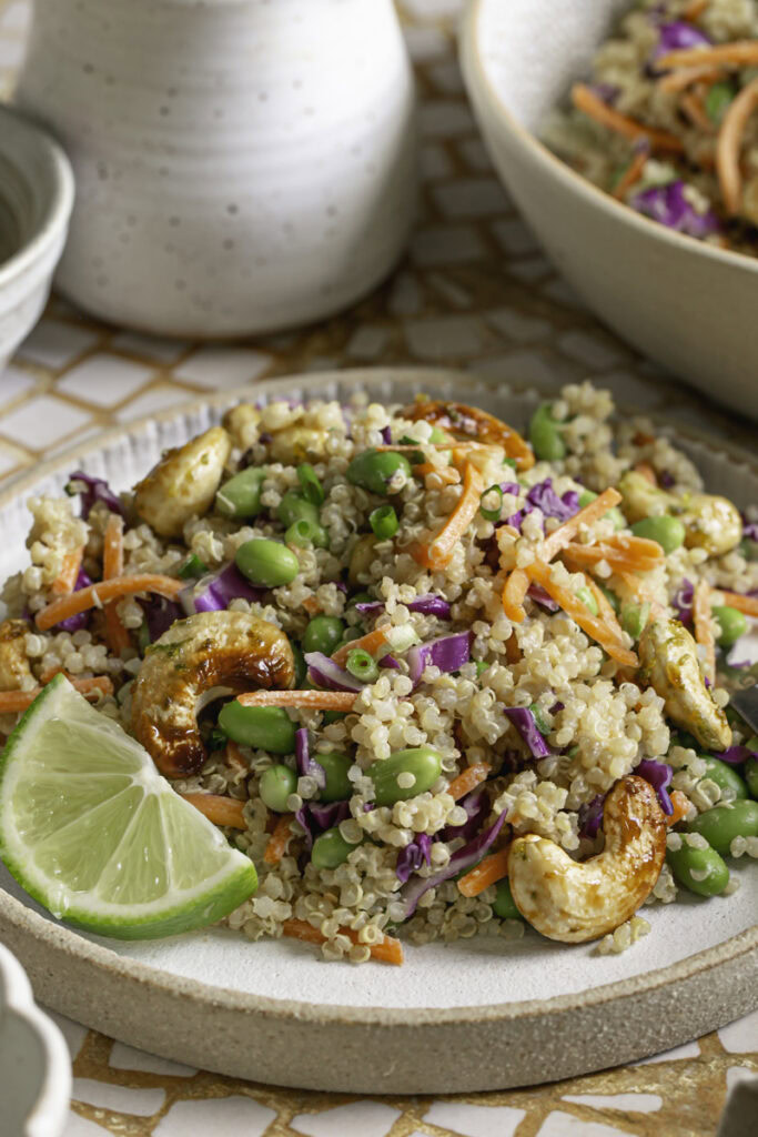 close up side shot of edamame quinoa salad on a plate with a lime slice.