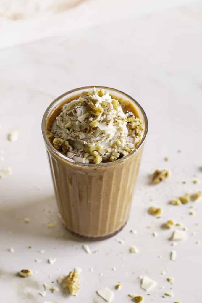 a 3/4 shot of carrot cake protein smoothie topped with oat whipped cream garnished with toasted coconut and chopped walnuts.