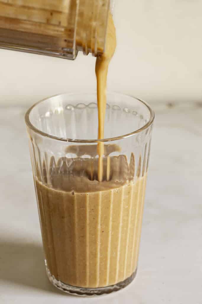 an action shot of pouring the carrot cake protein smoothie from the blender container into a glass.