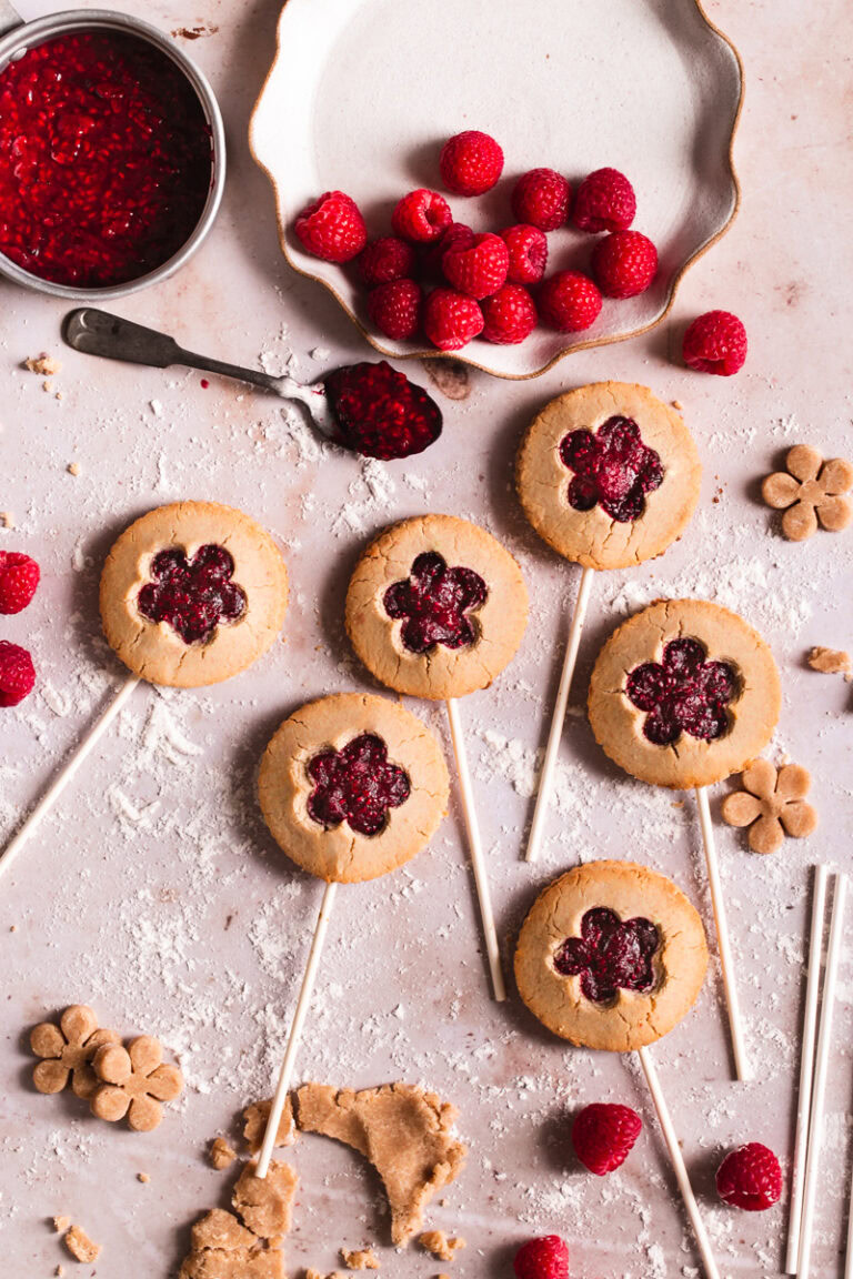 six raspberry pie pops laid out with a plate of fresh raspberries and a pot of raspberry jam beside it
