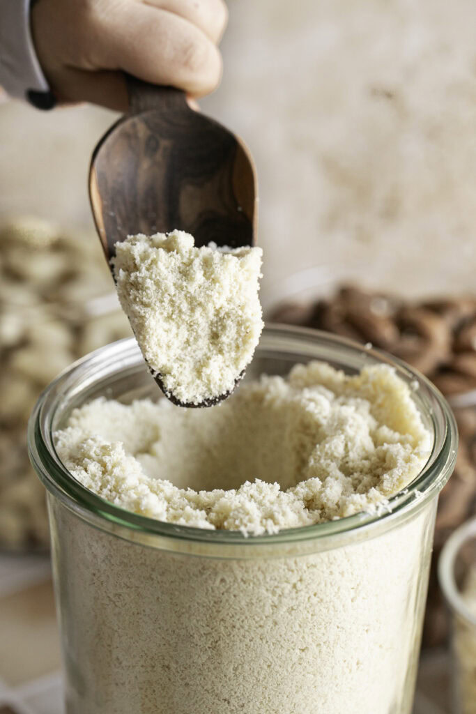 an action shot scooping almond flour out of a jar.