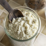 overhead shot of almond flour in a glass jar with a small wooden scoop.