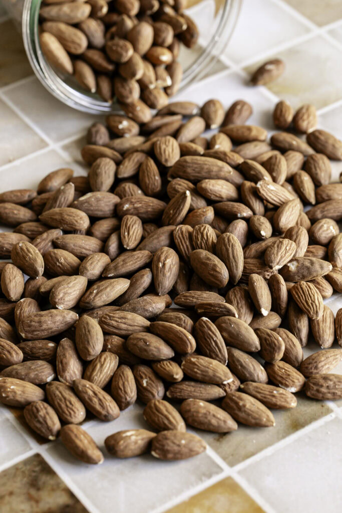 3/4 photo of whole almonds being poured out of a jar onto a table.