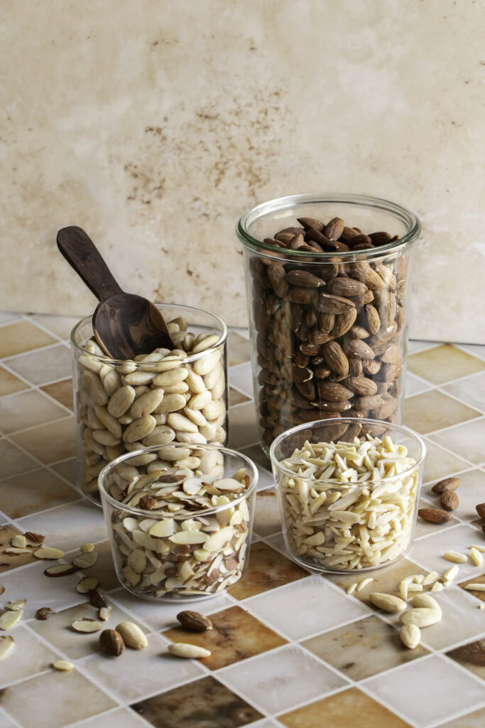 whole almonds, whole blanched almonds, sliced almonds, and slivered almonds in glass jars.