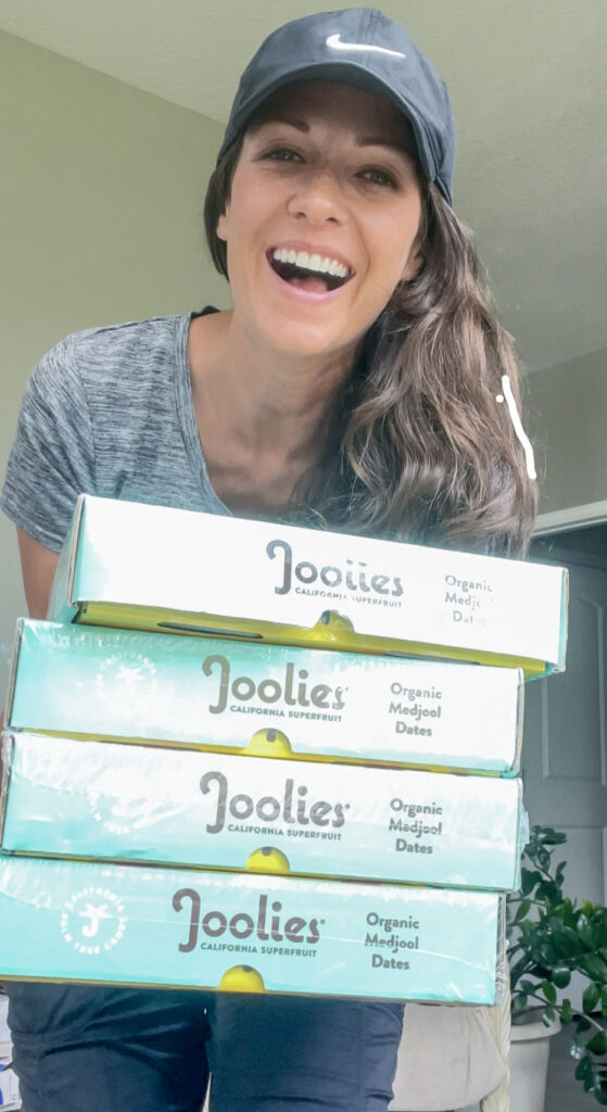 Gina Fontana smiling, holding 4 large boxes of Joolies dates.