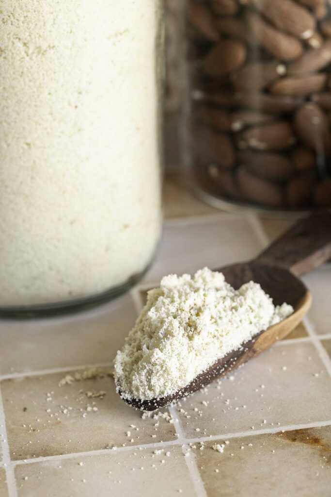 a scoop of almond flour in on the table in front of a jar of almond flour.