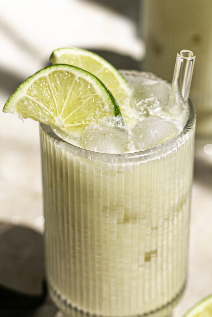 very close up shot of a glass of creamy coconut milk brazilian lemonade garnished with two lime slices and a glass straw sticking out of the glass.