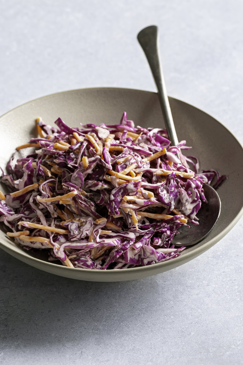 3/4 shot of red cabbage coleslaw in a bowl with a spoon in it.