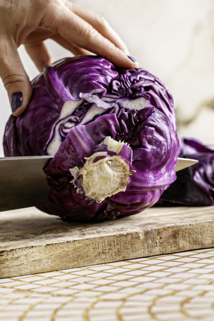 a close up image of a knife cutting off the root of the red cabbage.