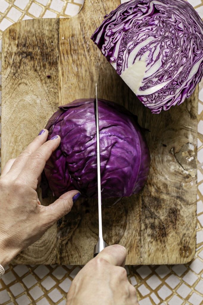 process shot of cutting the half of red cabbage in half again to cut the red cabbage into four quarters.