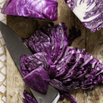 one quarter of the red cabbage sliced into pieces with the knife resting under the slices and the remaining half and quarter of red cabbage above it.