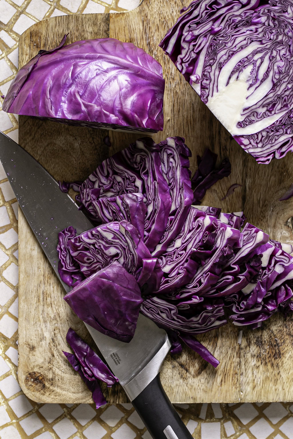 one quarter of the red cabbage sliced into pieces with the knife resting under the slices and the remaining half and quarter of red cabbage above it.