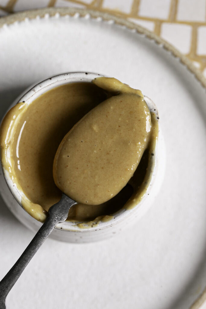 overhead photo of peanut ginger lime dressing on a spoon resting on a carafe filled with more dressing.