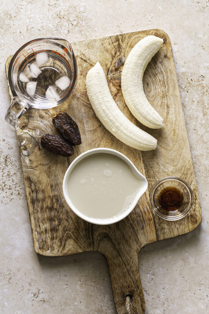 all the ingredients used to make banana milk on a wooden cutting board.