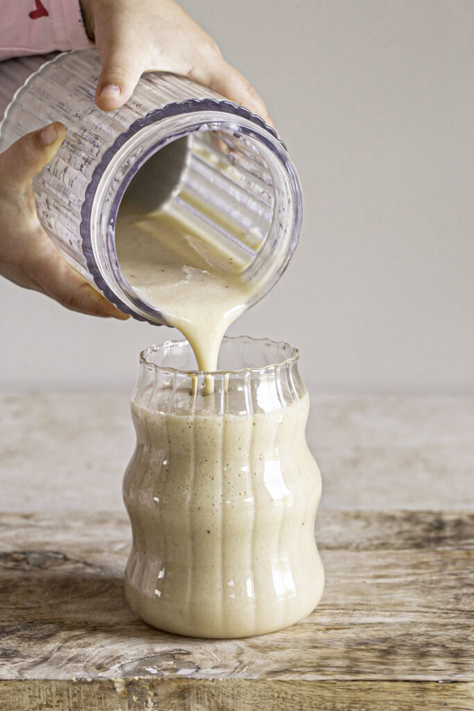action shot of pouring banana milk from the blender into a glass.