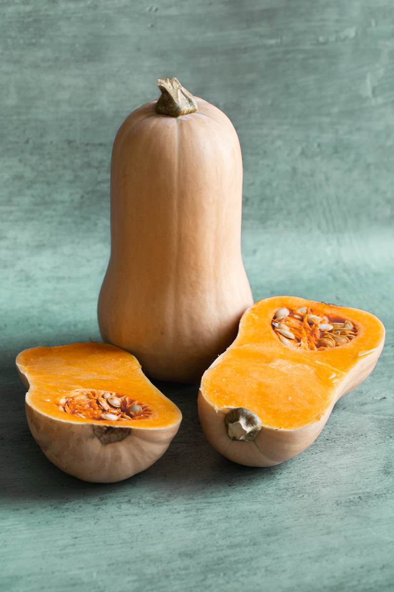 two butternut squash, one standing upward and the other cut in half to reveal the flesh and seeds laying down.