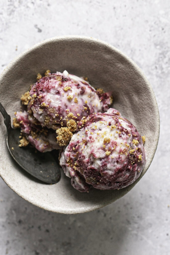 overhead shot of two scoops of blackberry cobbler ice cream in a bowl with a spoon.