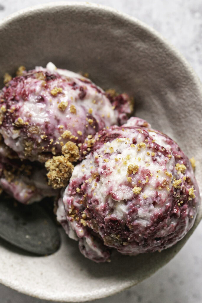 overhead shot of two scoops of blackberry cobbler ice cream in a bowl with a spoon.