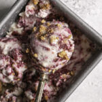 a scoop of blackberry cobbler ice cream in an ice cream scoop resting in a loaf pan of blackberry cobbler ice cream.